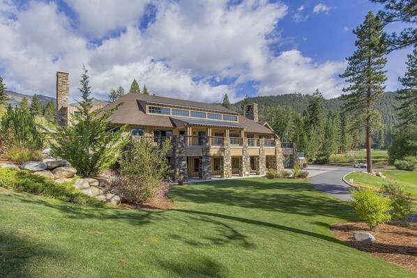 A large, multi-story house with a stone facade, multiple balconies, and a well-maintained lawn.