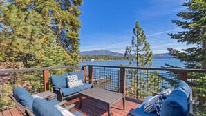 A deck with outdoor seating, overlooking a lake and forested mountains.