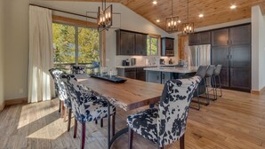 A modern kitchen with a wooden ceiling, a large island with bar stools, and a dining area with a cow-print table and chairs. - California Sunshine - Lakeview - TLUXP (Carnelian Bay)