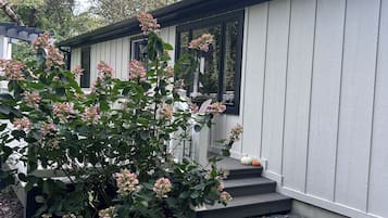 A modern house with a covered porch, a small garden with pink flowers, and a gravel driveway.