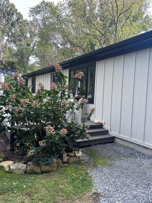 Een modern huis met een overdekte veranda, een kleine tuin met roze bloemen en een grindpad.