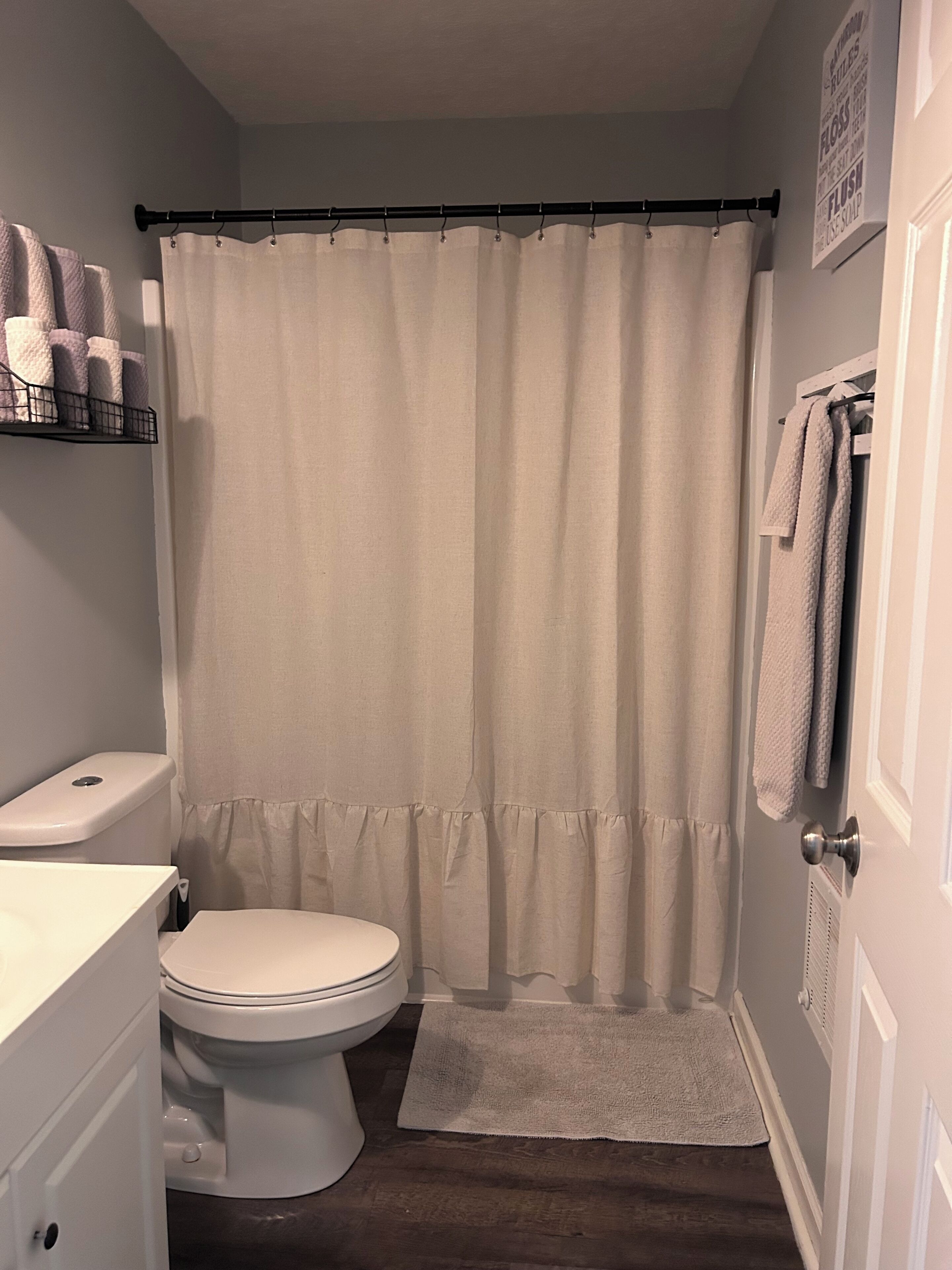 A bathroom with a toilet, a shower curtain, a towel rack, and a shelf with toiletries.