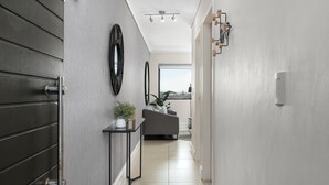 A modern hallway with a dark wooden door, a black-framed mirror, a small table with a plant, and a grey sofa in the background. - Water Edge 502 (Cape Town)