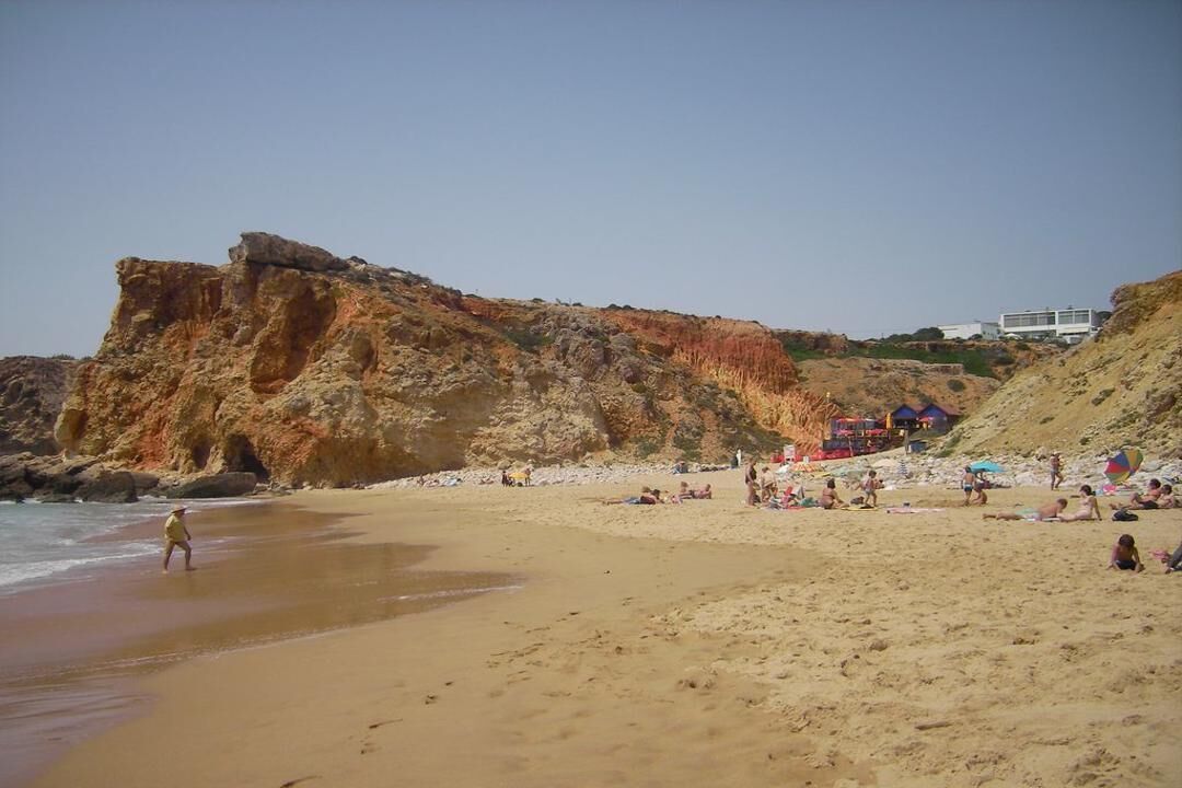 Une plage bordée de falaises rocheuses, avec une étendue de sable et quelques parasols.