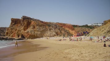 Une plage bordée de falaises rocheuses, avec une étendue de sable et quelques parasols.
