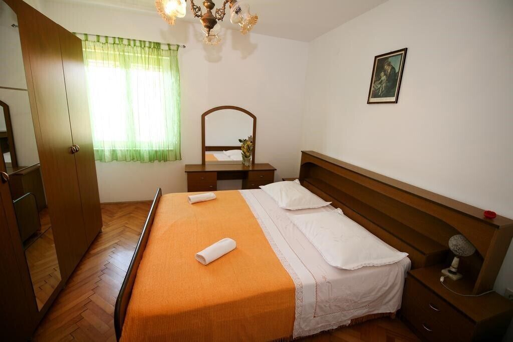 Een slaapkamer met een houten bed, nachtkastje, kaptafel, spiegel en een ingelijste foto aan de muur.