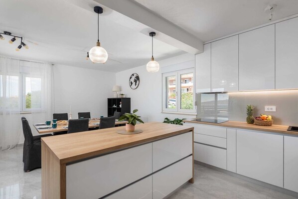 A modern kitchen with white cabinets, a wooden island, pendant lights, and a view of the outside.