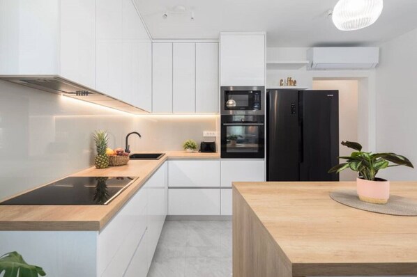 Una cocina moderna con armarios blancos, un refrigerador negro y una encimera de madera.