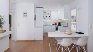 Une cuisine moderne avec des meubles blancs, un coin repas doté d’une table et de chaises blanches, et un micro-ondes visible.
