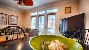 A dining area with a green bowl on a table, a ceiling fan, a TV, and a view through a glass door. - Blue Bliss - 6 Bedroom Beach House -1 Block from Beach Access. Linens Included! (Carolina Beach)