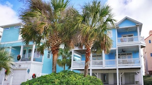 A two-story blue building with balconies, a garage, and palm trees. - Blue Bliss - 6 Bedroom Beach House -1 Block from Beach Access. Linens Included! (Carolina Beach)