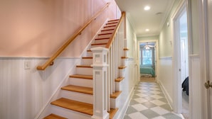 A staircase with wooden steps and white railings, leading to a room with a checkered floor and a bed with a green blanket. - Blue Bliss - 6 Bedroom Beach House -1 Block from Beach Access. Linens Included! (Carolina Beach)