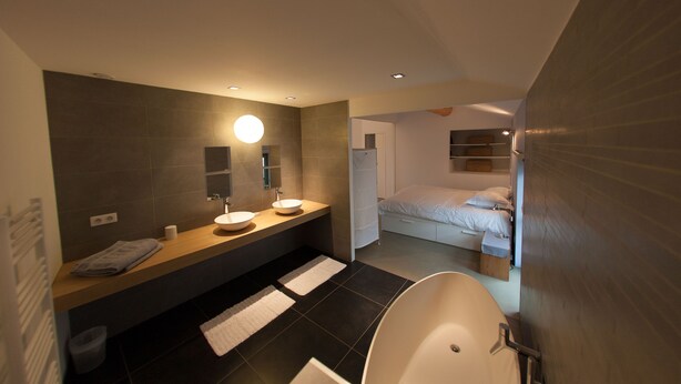 A modern bathroom with a large bathtub, a double sink vanity, and a separate bedroom area with a bed and nightstand. - Maison de Vacances Avec Piscine Privée Dans le Centre de Saint Rémy de Provence (Saint-Rémy-de-Provence)
