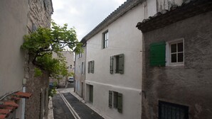 A narrow street flanked by buildings with green shutters, cobblestone pavement, and a tree with green leaves. - Maison de Vacances Avec Piscine Privée Dans le Centre de Saint Rémy de Provence (Saint-Rémy-de-Provence)