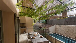 A dining area with a table set for four, a pool, and a covered outdoor space with a pergola. - Maison de Vacances Avec Piscine Privée Dans le Centre de Saint Rémy de Provence (Saint-Rémy-de-Provence)
