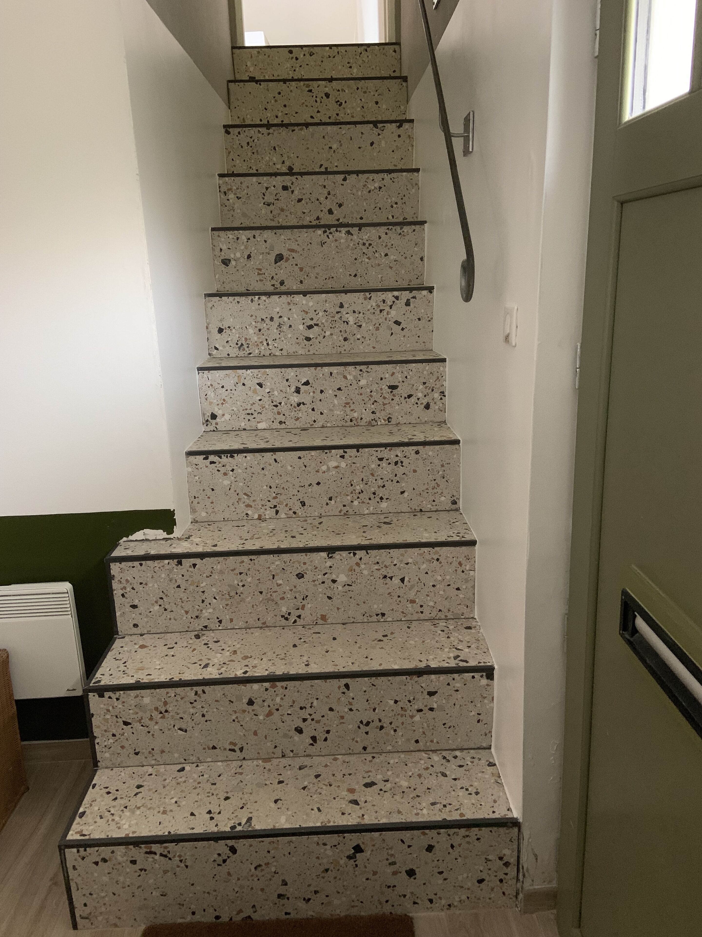 A staircase with a terrazzo finish, leading to a room with a green wall and a white radiator.