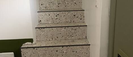 A staircase with a terrazzo finish, leading to a room with a green wall and a white radiator.