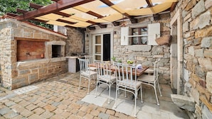A stone-built outdoor patio with a brick floor, a wooden table, and white metal chairs. - Rustic Villa Katarina Gračišće with pools and a sauna (Gracisce)