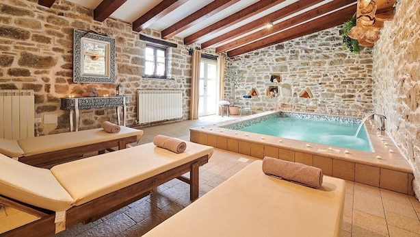 A stone-walled room with a large bathtub, wooden benches, and a massage table. - Rustic Villa Katarina Gračišće with pools and a sauna (Gracisce)