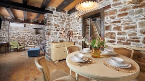 A rustic stone-walled dining area with a round table set for four, a vase of flowers, and a wooden cabinet. - Rustic Villa Katarina Gračišće with pools and a sauna (Gracisce)