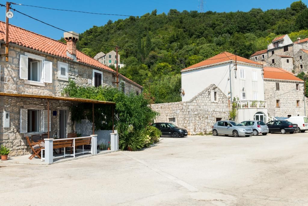 A stone building with a red-tiled roof, a bench outside, and several parked cars.
