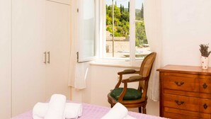 A bedroom with a bed, a chair, a dresser, and a window with a view of greenery. - Holiday Home Anima Maris (Ston)