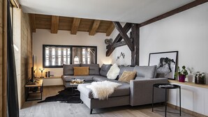 Una sala de estar moderna con un sofá seccional gris, vigas de madera, un cuadro con marco negro y una pequeña mesita auxiliar.
