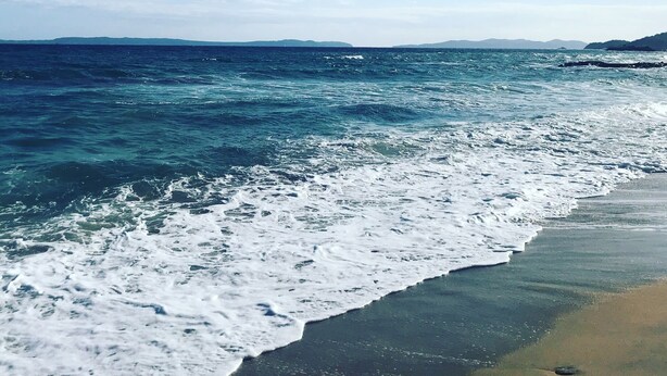 Ein Strand mit Wellen, blauem Himmel und Bergen in der Ferne.