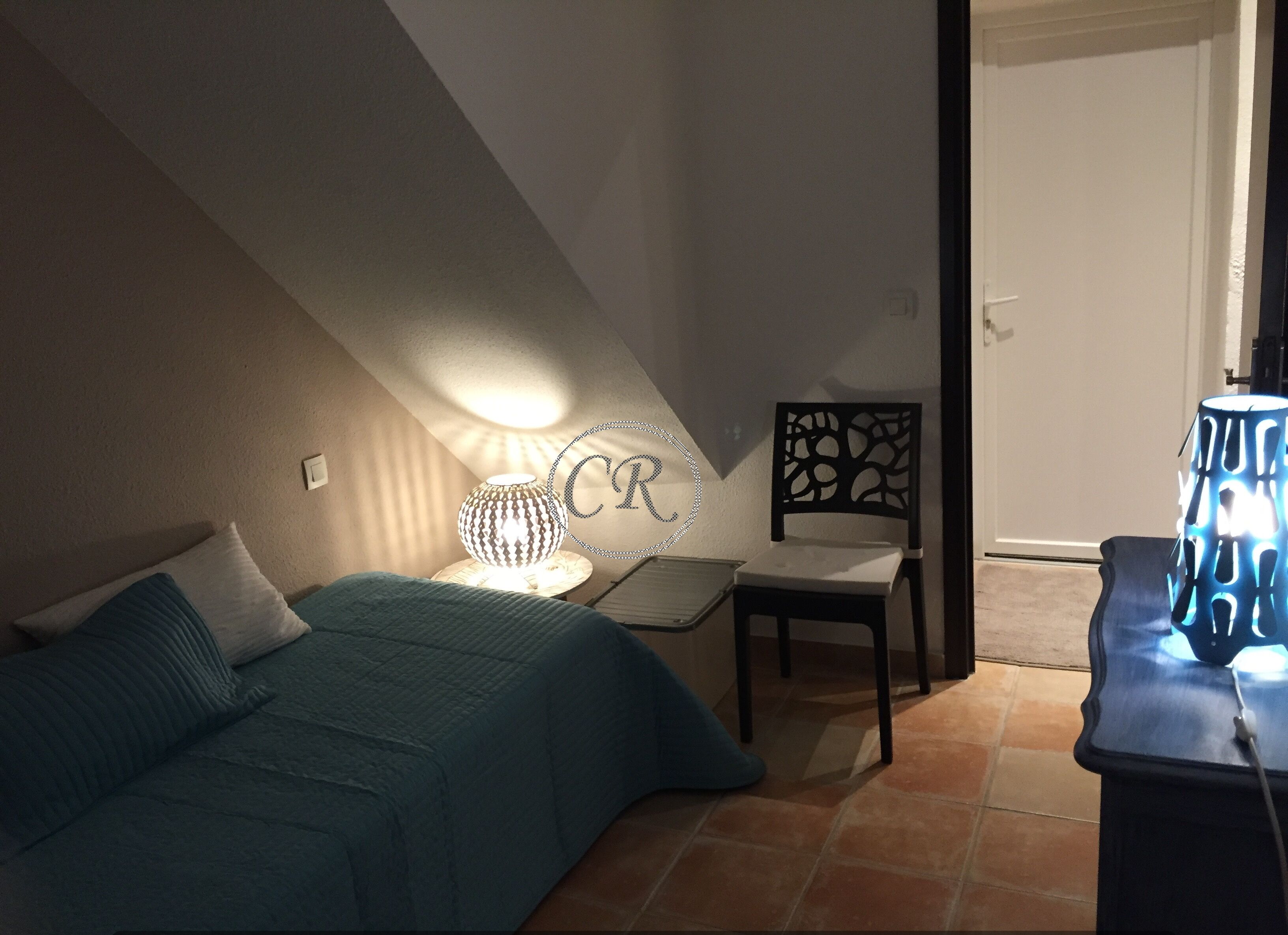 A bedroom with a bed, a chair, a desk, and a lamp.