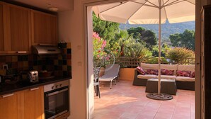 Eine Küche mit Holdekor und einem modernen Herd, die auf eine Terrasse mit Esstisch, Stühlen und einem großen Sonnenschirm führt.