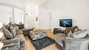 A modern living room with a sofa set, ottoman, and a flat-screen TV. - 418 - Fabulous 4 Bed Home with South Facing Pool and Spa (Davenport)
