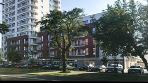 Een meerlaags woongebouw met balkons, een parkeerplaats met auto's en bomen ervoor.