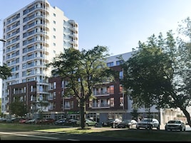 Un edificio residencial de varios pisos con balcones, un estacionamiento con coches y árboles en la parte delantera.