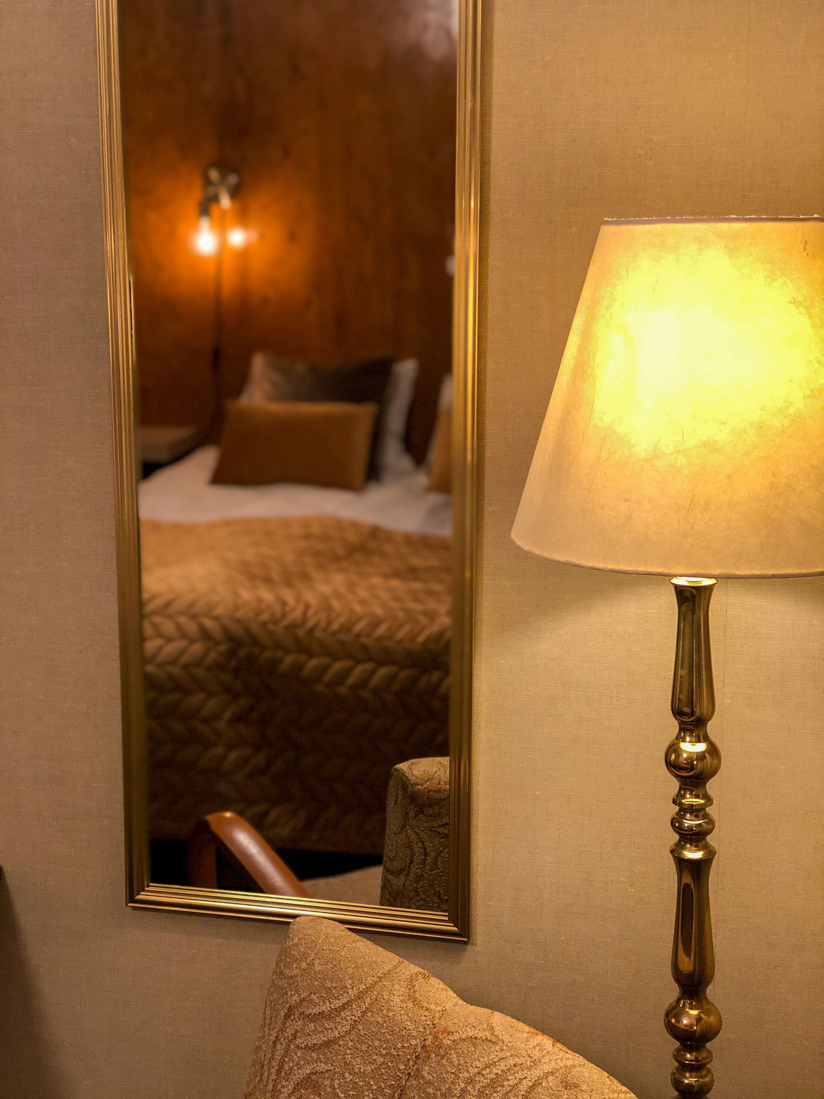 Une pièce comprenant un lit, une lampe et un miroir qui reflète le lit et une table de chevet.