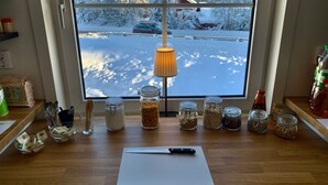 Eine Küchenarbeitsfläche mit verschiedenen Gewürzgläsern, einem Schneidebrett und einem Fenster mit Blick auf Schnee.