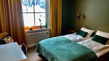 A bedroom with a bed, a desk, a window with curtains, and a radiator.