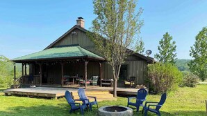A rustic wooden building with a covered porch, outdoor seating area with chairs, and a fire pit. - Rustic Cabin, Wood Fireplace & Large Deck (Great Valley)