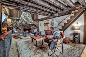 Ein rustikales Interieur mit Kamin aus Stein, Holzbalken, einem Ledersofa und einer Treppe.