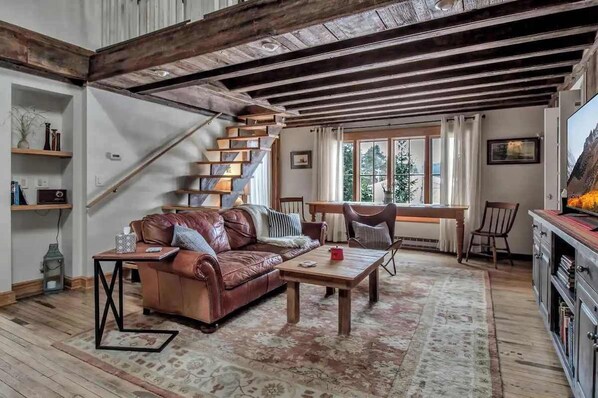 Ein rustikales Wohnzimmer mit Ledersofa, Holztisch und einer Treppe mit Holzbalken.