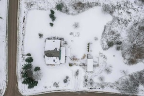 Eine Vogelperspektive auf ein Anwesen mit einem großen Gebäude, mehreren kleineren Strukturen und einer schneebedeckten Landschaft mit Bäumen.