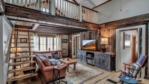 A spacious living area with a wooden staircase, a sofa, a television, and a dining table. - Rustic Cabin, Wood Fireplace & Large Deck (Great Valley)