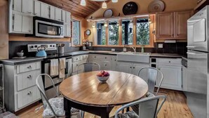 A kitchen with white cabinets, a microwave, a stove, a sink, and a dining table with chairs. - Rustic Cabin, Wood Fireplace & Large Deck (Great Valley)