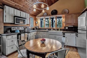 A kitchen with white cabinets, a microwave, a stove, a sink, and a dining table with chairs.