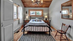 A bedroom with a bed, a chandelier, a window, a chair, and a mirror. - Rustic Cabin, Wood Fireplace & Large Deck (Great Valley)