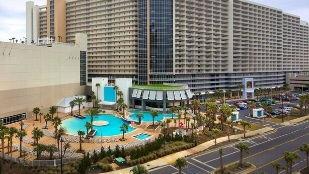 Un gran hotel con varios pisos, un patio central con piscina y un estacionamiento con varios coches.