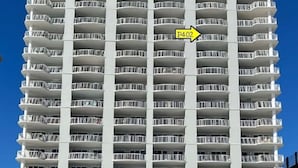 A high-rise hotel with multiple balconies, a clear blue sky, and a sandy ground. - Premiere Complex. Beachfront Penthouse Unit W/ Amazing View, Extra Large Balcony (Gulf Shores)