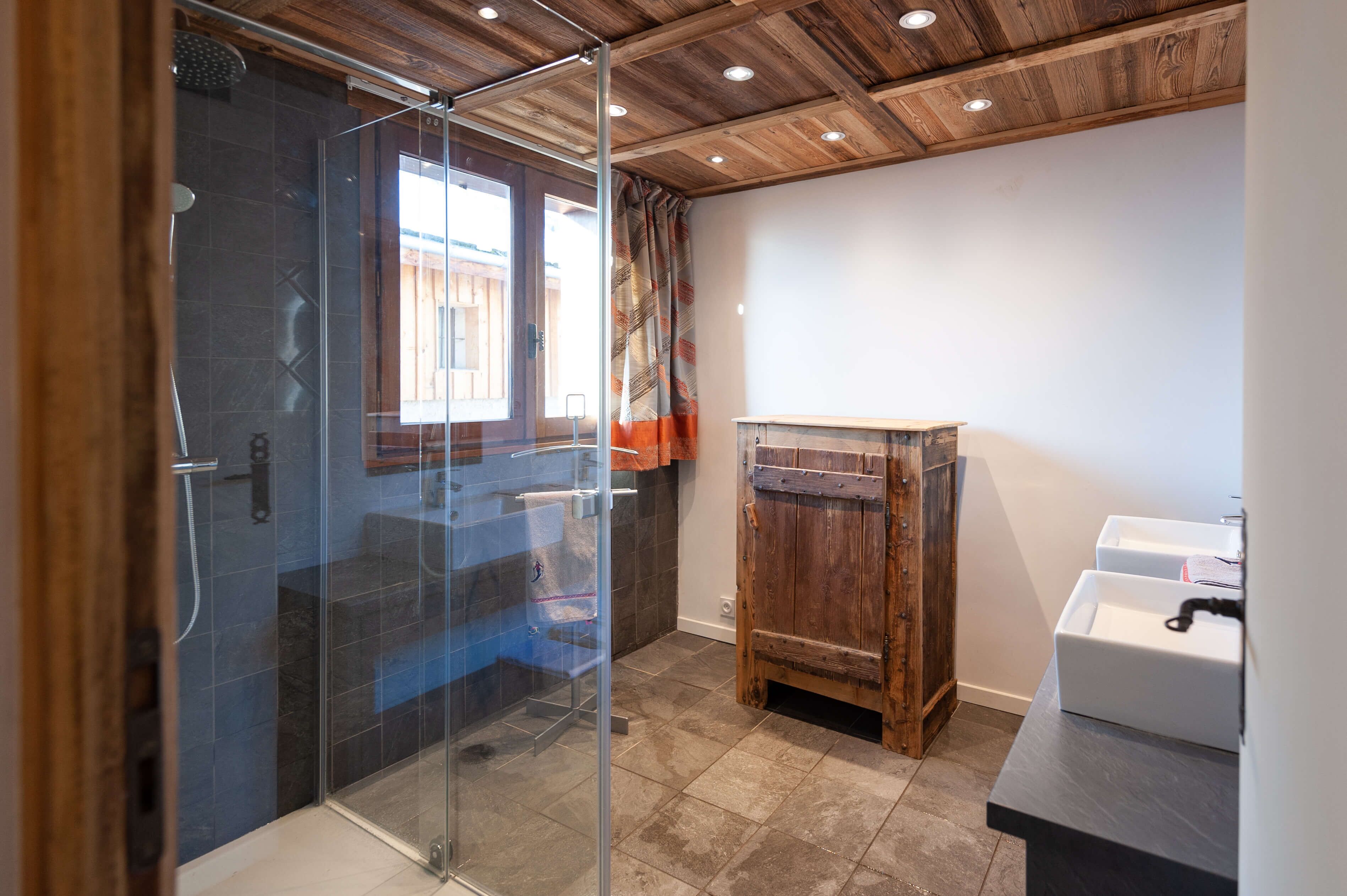 A modern bathroom with a glass shower enclosure, a wooden cabinet, and a sink.