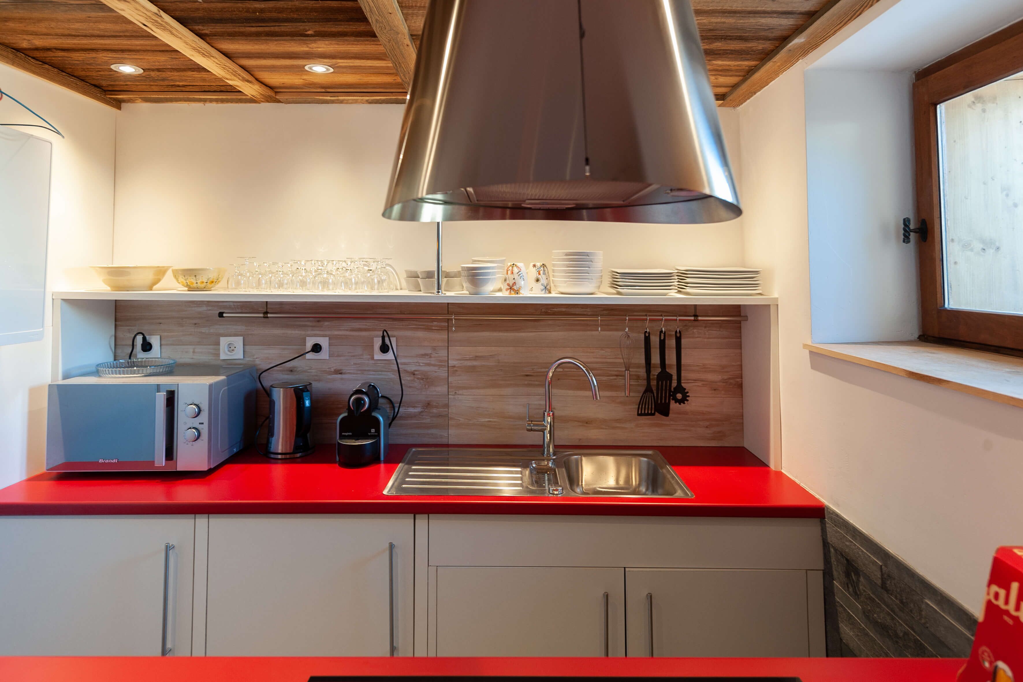 A modern kitchen with a red countertop, stainless steel appliances, and wooden cabinetry.