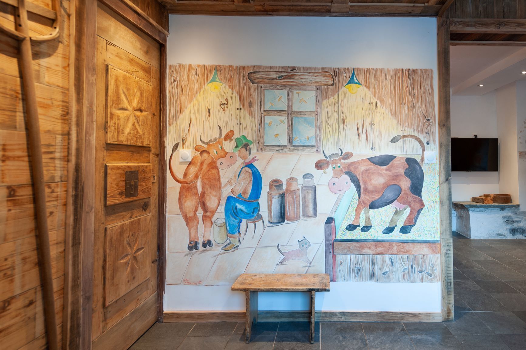 Un intérieur rustique avec un mur en bois et une fresque représentant une scène avec des vaches et une personne.