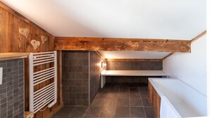 A compact bathroom with wooden beams, a white bathtub, and a towel rack. - Chalet Marcel et Grégoire (Les Belleville)